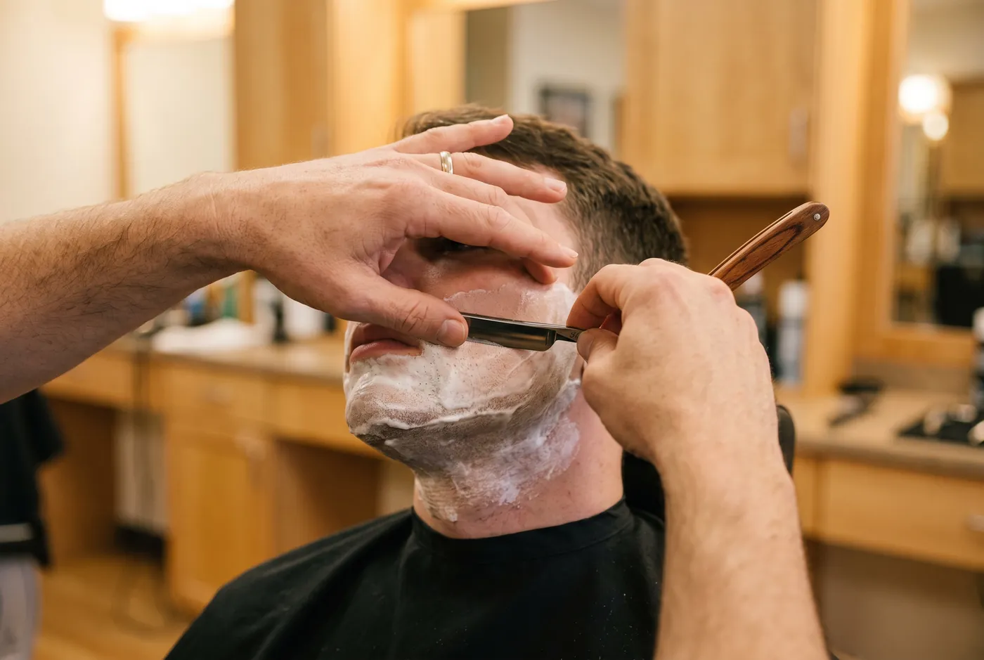 Close-up of a straight razor shave, one hand stretching the skin of a lathered cheek